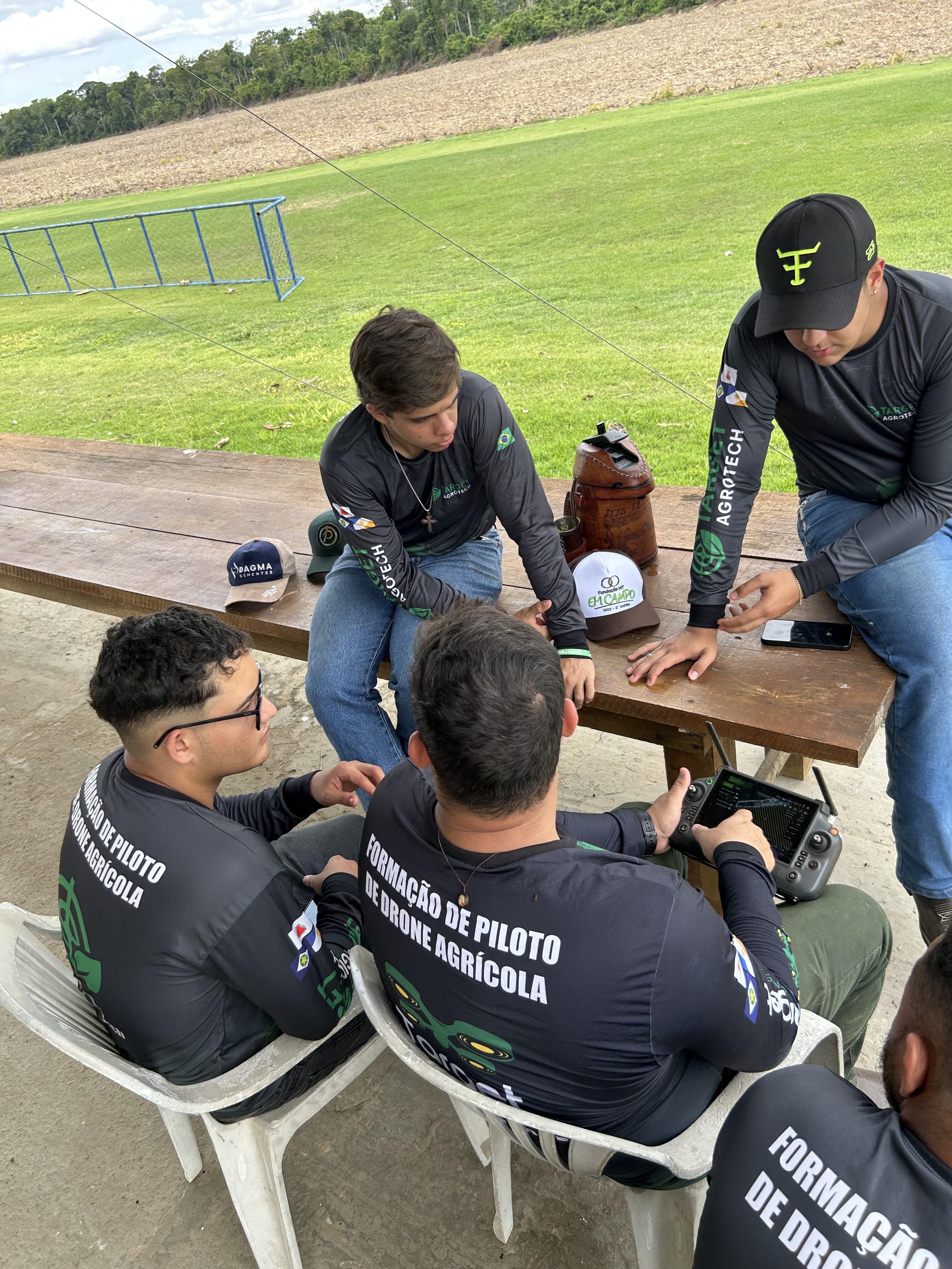 Alunos sentados à mesa revisando configurações e rotas de voo do drone agrícola